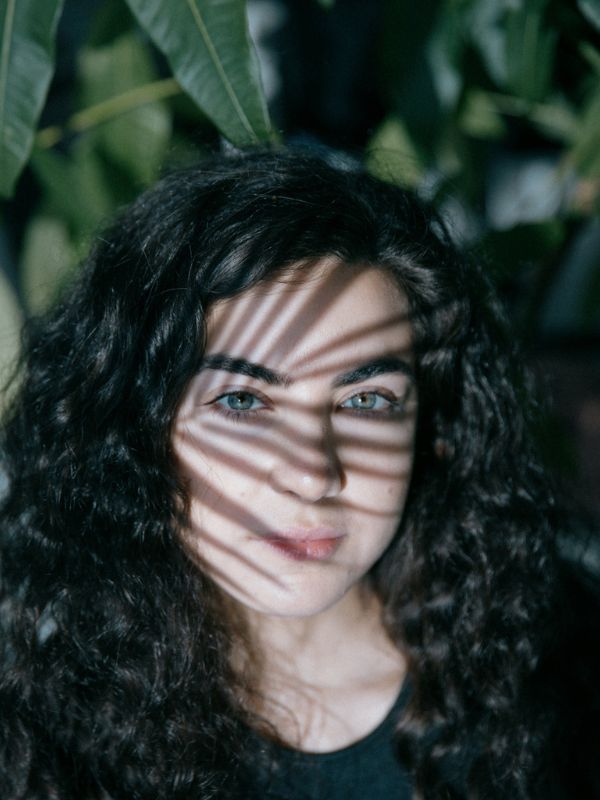 A woman looks at the camera with the shadow of a leaf on her face.