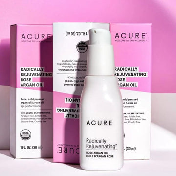 A pump bottle of ACURE Radically Rejuvenating Rose Argan Oil with its packaging box displayed against a pink & white background.