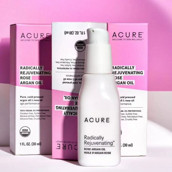 A pump bottle of ACURE Radically Rejuvenating Rose Argan Oil with its packaging box displayed against a pink & white background.