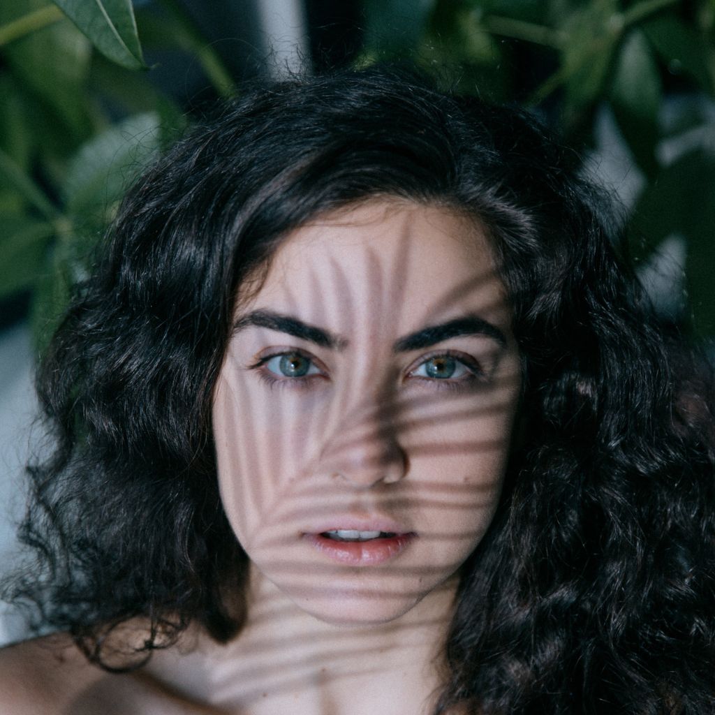 woman looks forward with the shadow of a plant leaf on her face