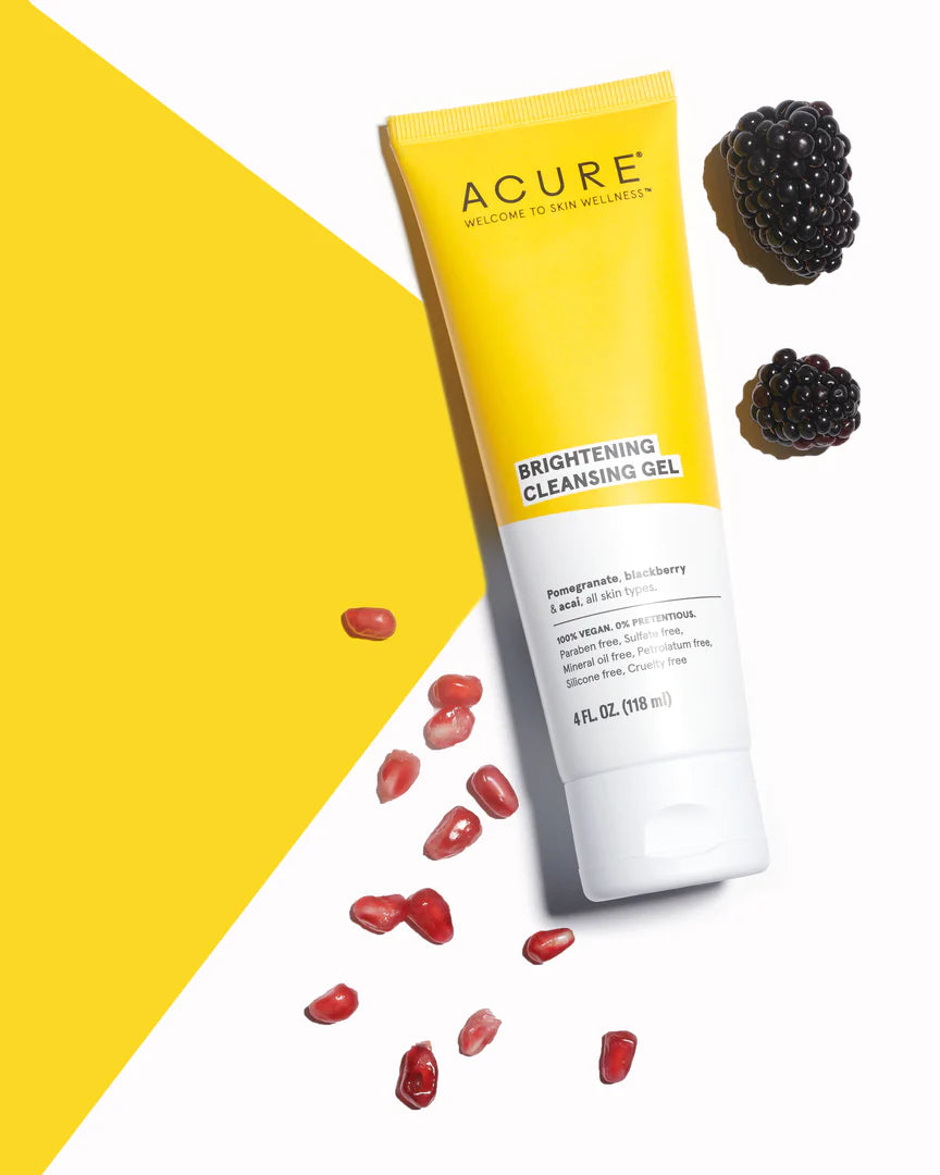 Acure Brightening Cleansing Gel tube with pomegranate seeds and blackberries on a yellow and white background.