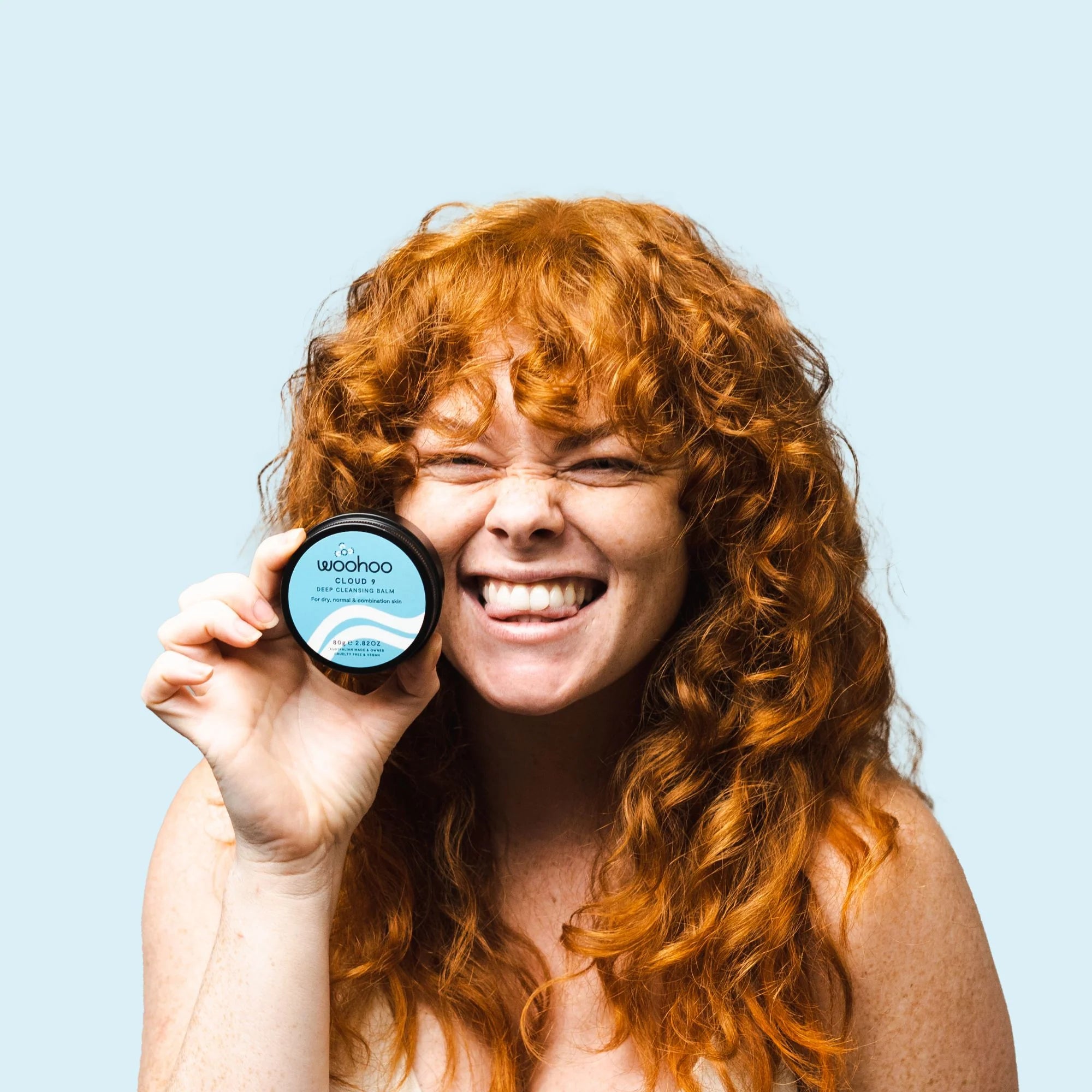 Image of a redheaded woman holding the Woohoo Cloud 9 Deep Cleansing Balm Tin next to her face as she is smiling at the camera.