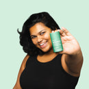 Woman holding Woohoo best-selling WILD Natural Deodorant Stick in front of a light green background